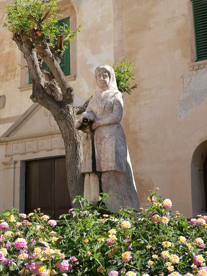 Sculpture of a woman in front of the facade of the medieval church of Felanitx.
