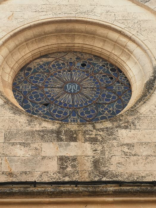 Big round rosette window with stained glass in the facade of convent Monestir Concepcionista in Sineu, Mallorca.