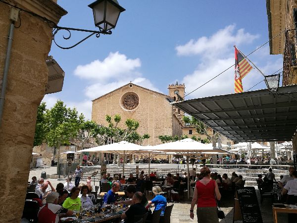 Crowded bars at the main square of Pollenca old town, Mallorca, with the parish church in the background.