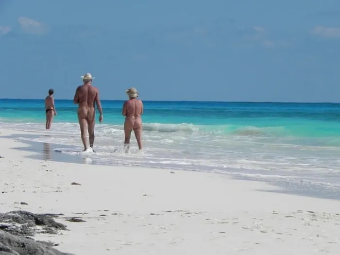 Three nudists walking on a beach in Mallorca, Spain on a sunny summer day.