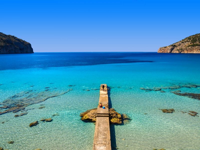 Jetty extending from a beach in a cove surrounded by rocky cliffs in Camp de Mar resort, Mallorca island, Spain.