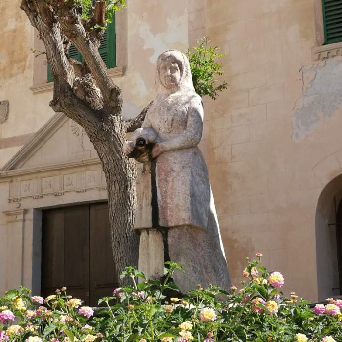 Sculpture of a woman in front of the facade of the medieval church of Felanitx.