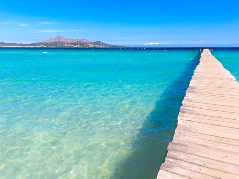Turqoise shallow waters at the beach and bay of Platja de Muro resort, Mallorca island, Spain.